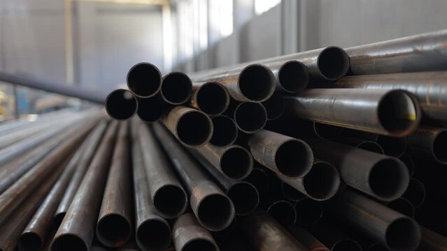 Numerous metal pipes with big diameter stacked in pile at spacious warehouse of modern industrial factory. Round construction materials waiting for shipment as intended. Concept of Industry.
