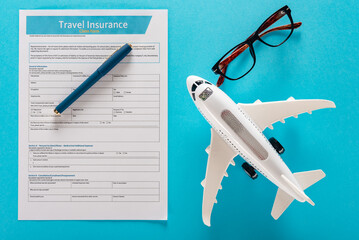 Flat lay of worldwide travel insurance form, pen, glasses and air plane