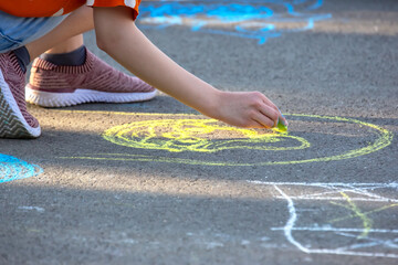 The girl draws a smiley face with yellow chalk on the pavement. Creativity and hobbies of children entertainment and recreation - obrazy, fototapety, plakaty