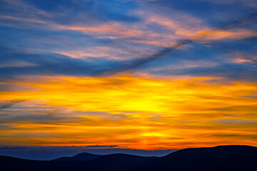 Colorful clouds in the sky at sunset against the backdrop of a mountainous forest area.