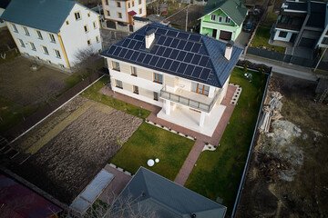 Aerial drone view of house with photovoltaic solar panels on rooftop surrounded by yard, road and...