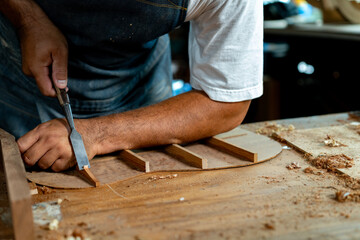 Close-up of guitar luthier using chisel to shave bracing of acoustic guitar.