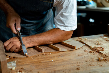Close-up of guitar luthier using chisel to shave bracing of acoustic guitar.