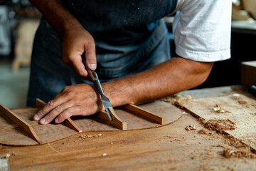 Close-up of guitar luthier using chisel to shave bracing of acoustic guitar. - obrazy, fototapety, plakaty