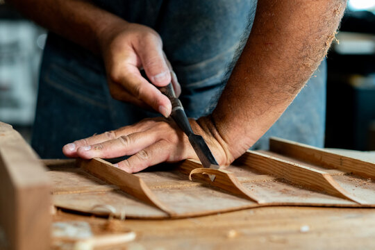 Close-up of guitar luthier using chisel to shave bracing of acoustic guitar.