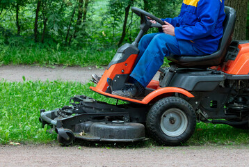 A lawnmower mows the grass in the park