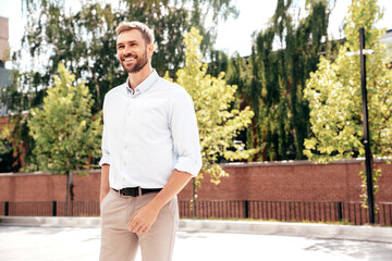 Handsome smiling stylish hipster lambersexual model. Modern man dressed in white shirt and trousers. Fashion male posing in the street background