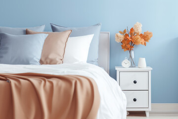 Modern minimalist bedroom interior in blue tones. A bouquet of dry hydrangea and autumn leaves in a vase on the bedside table.