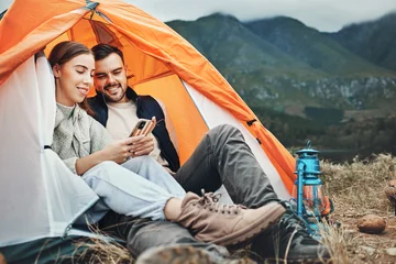 Foto op Canvas Couple, tent and camping with phone, smile and reading for holiday, web blog and morning in countryside. Man, woman and relax with vacation, social media and adventure with love, outdoor and freedom © Rene L/peopleimages.com