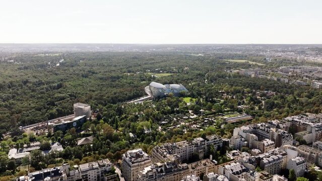 Aerial panoramic view of large green park in city. Art design building of Fondation Louis Vuitton in Bois de Boulogne. Paris, France