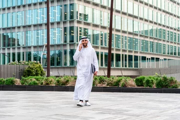 Fototapeten Arab middle-eastern man wearing emirati kandora traditional clothing in the city - Arabian muslim businessman strolling in urban business centre. © oneinchpunch