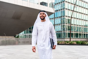 Gartenposter Arab middle-eastern man wearing emirati kandora traditional clothing in the city - Arabian muslim businessman strolling in urban business centre. © oneinchpunch
