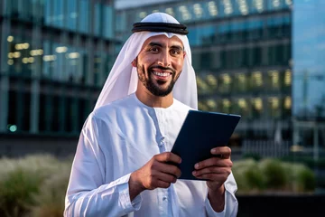 Tuinposter Arab middle-eastern man wearing emirati kandora traditional clothing in the city - Arabian muslim businessman strolling in urban business centre. © oneinchpunch