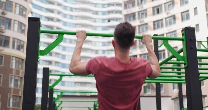 Athletic man doing pull-ups at outdoor gym, back view. Camera moving right