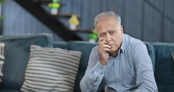 Asian Hindu Indian tired old aged sad upset man sitting alone on sofa couch feel bad indoor home older elder adult gen x lonely stress unwell male suffer health issue living room house