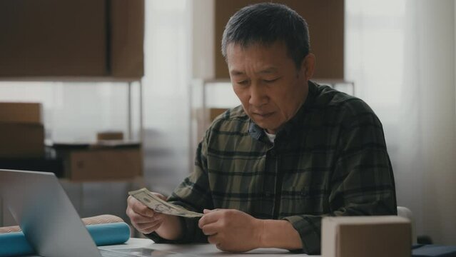 Upset Asian male entrepreneur counts last money in office, debts, bankruptcy