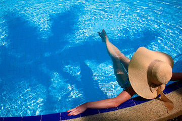 Beautiful woman in kraft hat by the pool enjoying the tropical climate. The concept of travel, relaxation and enjoying life.