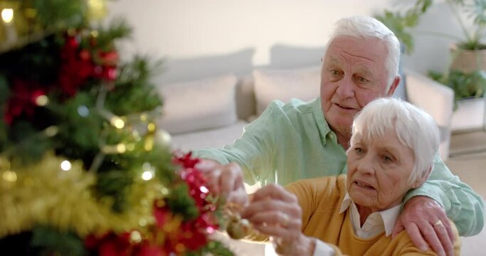 Happy senior caucasian couple decorating christmas tree at home, slow motion - Powered by Adobe