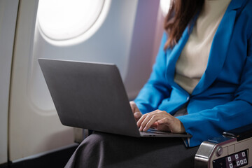 Asian young woman using laptop sitting near windows at first class on airplane during...