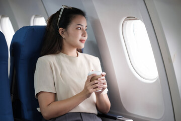 A female tourist is sitting inside a passenger plane, looking at the bird's eye view from the airplane window.