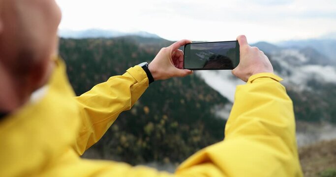Photographer tourist blogger holds a mobile phone in hands takes pictures on smartphone autumn foggy mountain. Tourist shooting on the phone and mountain panorama