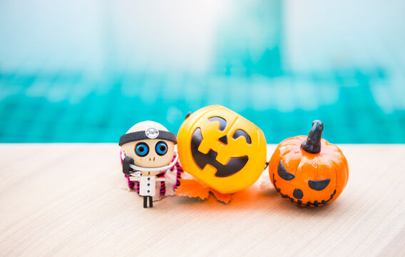 Little doctor ghost wooden doll and Halloween pumpkin on swimming pool edge, outdoor day light, Halloween background idea