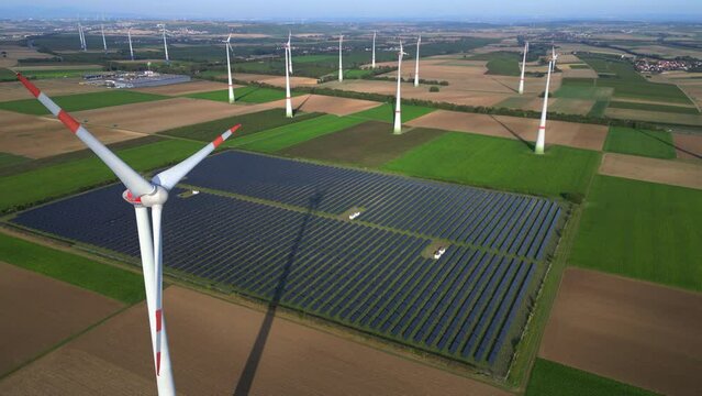 Rotierende Windturbine im Windpark vor Solarpark im Hintergrund in l&auml;ndlicher Umgebung als Luftaufnahme