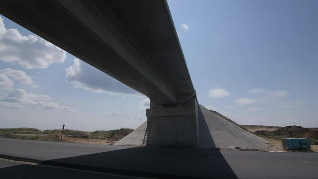 Car drives under incomplete traffic overpass at construction site. Transport bridge over highway structure improvement. Freeway maintenance
