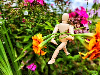 Wooden toy man with flowers against background grass in nature. Concept of holiday, gift bouquet,...
