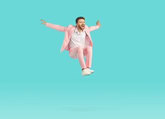 Funny guy with unshaven beard wearing stylish bright pink suit jumping high isolated on blue...