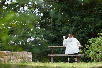 Fototapeta premium 秋の公園のベンチで休憩している若い女性の後姿