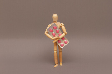 Wooden figurine holding a blister with pink pills.
