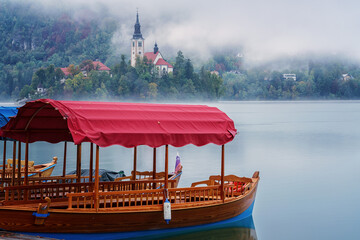 Famous alpine Bled lake (Blejsko jezero) in dense fog, amazing misty landscape, Slovenia. Scenic view of the lake with wooden pleasure boats and island with church, outdoor travel background