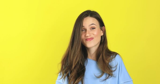 Shocked smiling shy charming confused young woman in blue sweater posing isolated on yellow background studio. Girl looking at camera smile cover mouth with hand say oops.