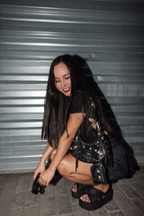 Fototapeta na wymiar Beautiful happy fashion young woman model in fashionable clothes with top and skirt with slippers with stylish handbag sitting and having fun on the street at night