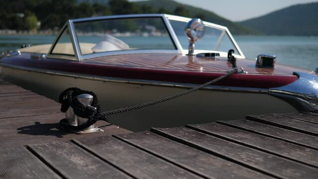 View of a speedboat moored to the pier and bobbing on the waves of the lake in the evening, the boat is tied with a rope to a wooden pier. A small luxury pleasure boat moored to a pier on a small lake