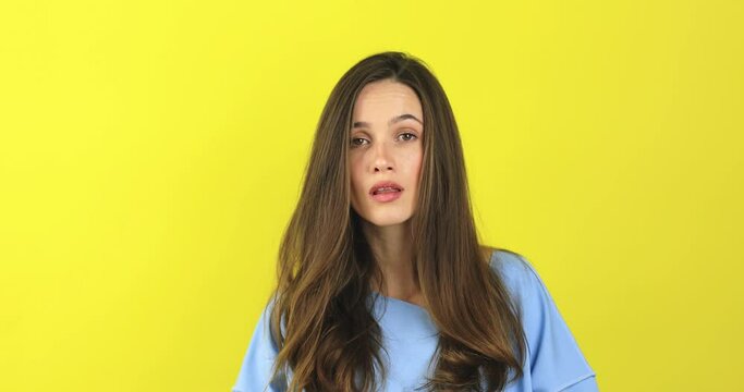 Brunette curly woman threatens with a fist is isolated on yellow background, shows fist has annoyed face expression going to revenge or threaten someone makes serious look. I will show you who is boss