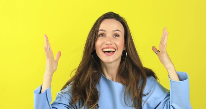 Happy woman looking camera shocked surprised say wow put hands on face, touch her hair. Wow, it is awesome. Surprised girl face. Close up of shocked woman face expression isolated on yellow background