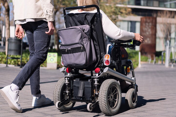 cropped rear view of an unrecognizable woman using wheelchair with a man taking a walk by the city,...