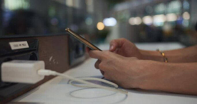 Woman traveler charging mobile phone at charging station at airport departure terminal. Close-up shot