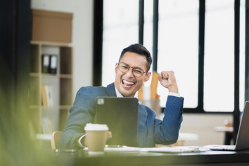 Excited man work distant on computer talk on cellphone celebrate online win. Happy young male use laptop feel euphoric overjoyed triumph with good news over smartphone call.