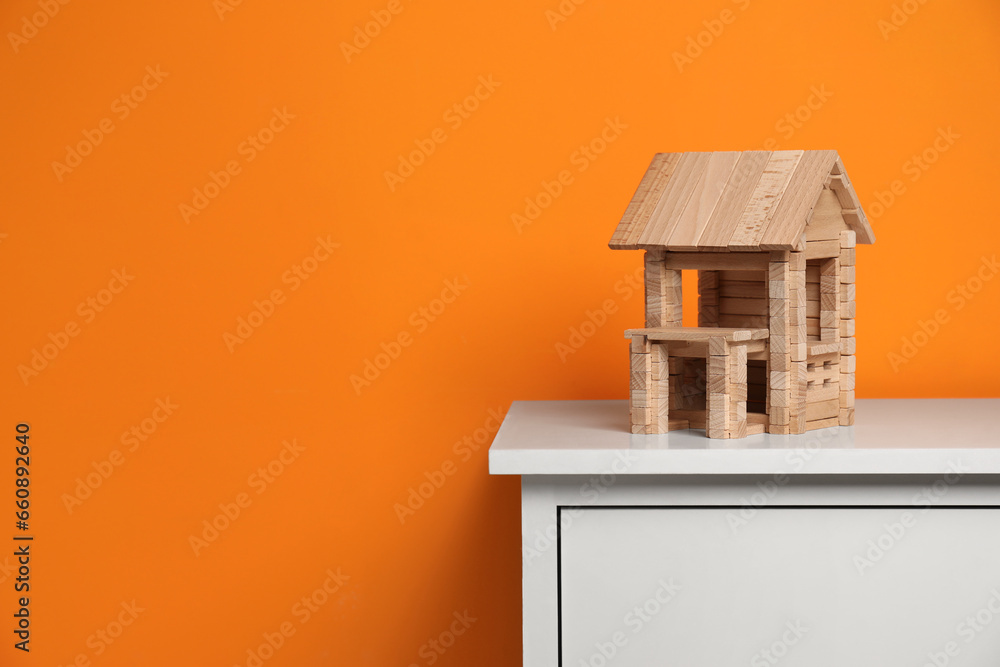 Wall mural Wooden house on white chest of drawers near orange wall, space for text. Children's toy