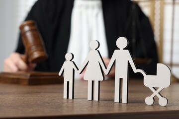 Family law. Judge with gavel sitting at wooden table, focus on figure of parents and children - obrazy, fototapety, plakaty