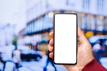 Mockup blank white screen of smartphone, male hand holding modern black cellphone with template screen for your logo or design,city blurred street in the background.