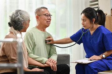 Fototapeta premium Female doctor using stethoscope examining senior male during home care visit. Elderly healthcare concept