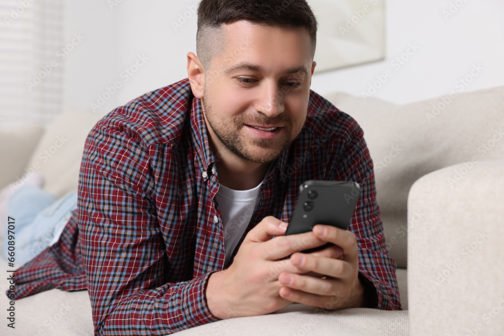 Poster handsome man sending message via smartphone on sofa at home