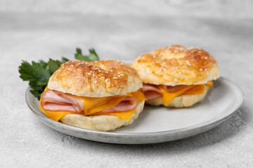 Delicious bagels with ham and cheese on light table, closeup