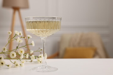 Glass of alcohol drink and flowers on table in room, space for text. Relax at home