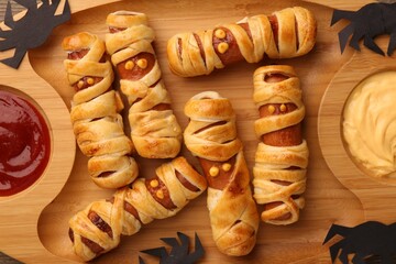 Cute sausage mummies served with sauce on wooden table, closeup. Halloween party food