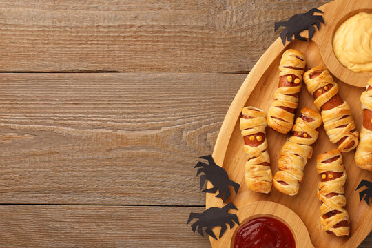 Cute sausage mummies served with sauce on wooden table, top view with space for text. Halloween party food